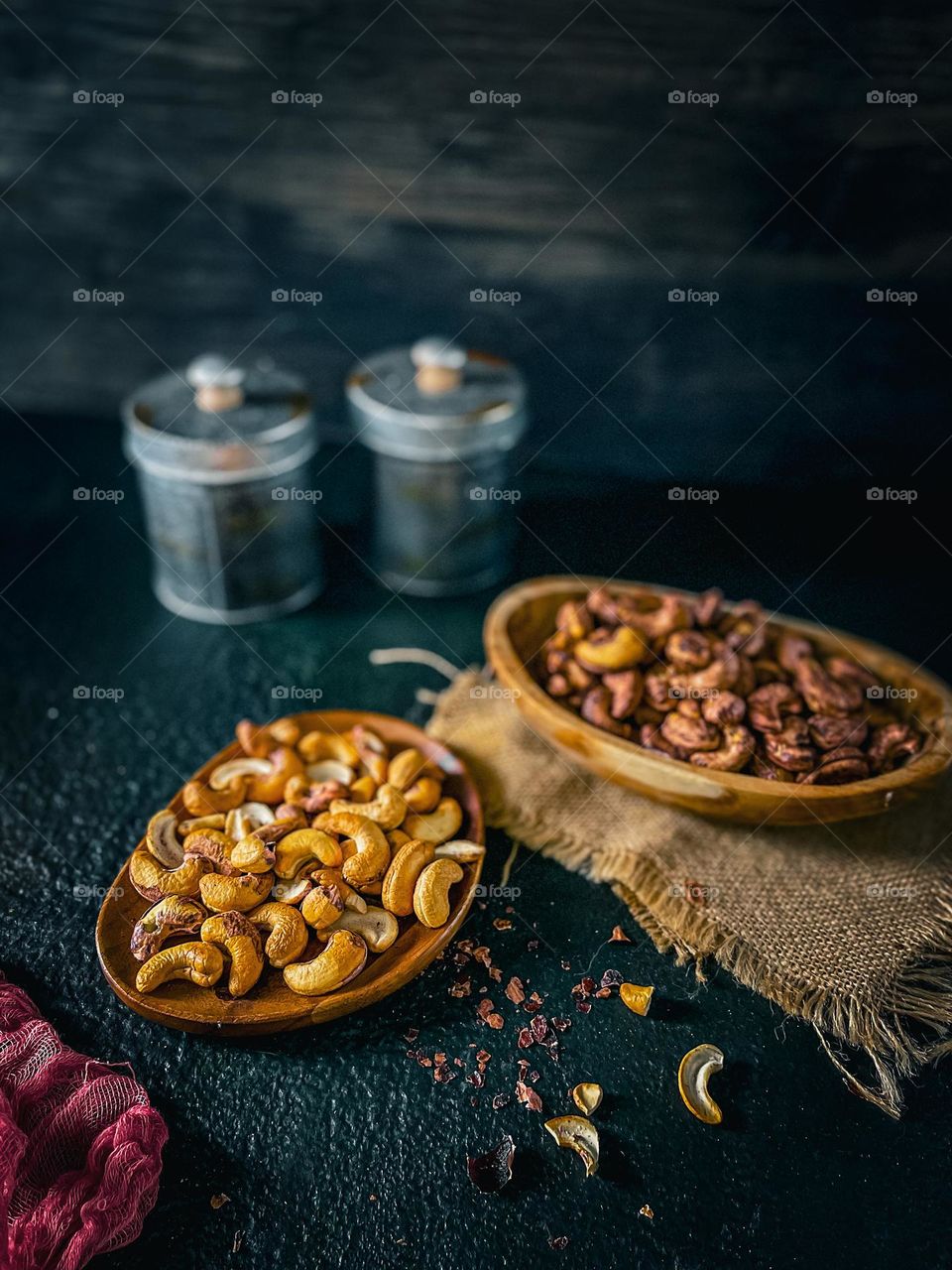 Cashew nuts in a wooden bowl and plate and some canisters at the back