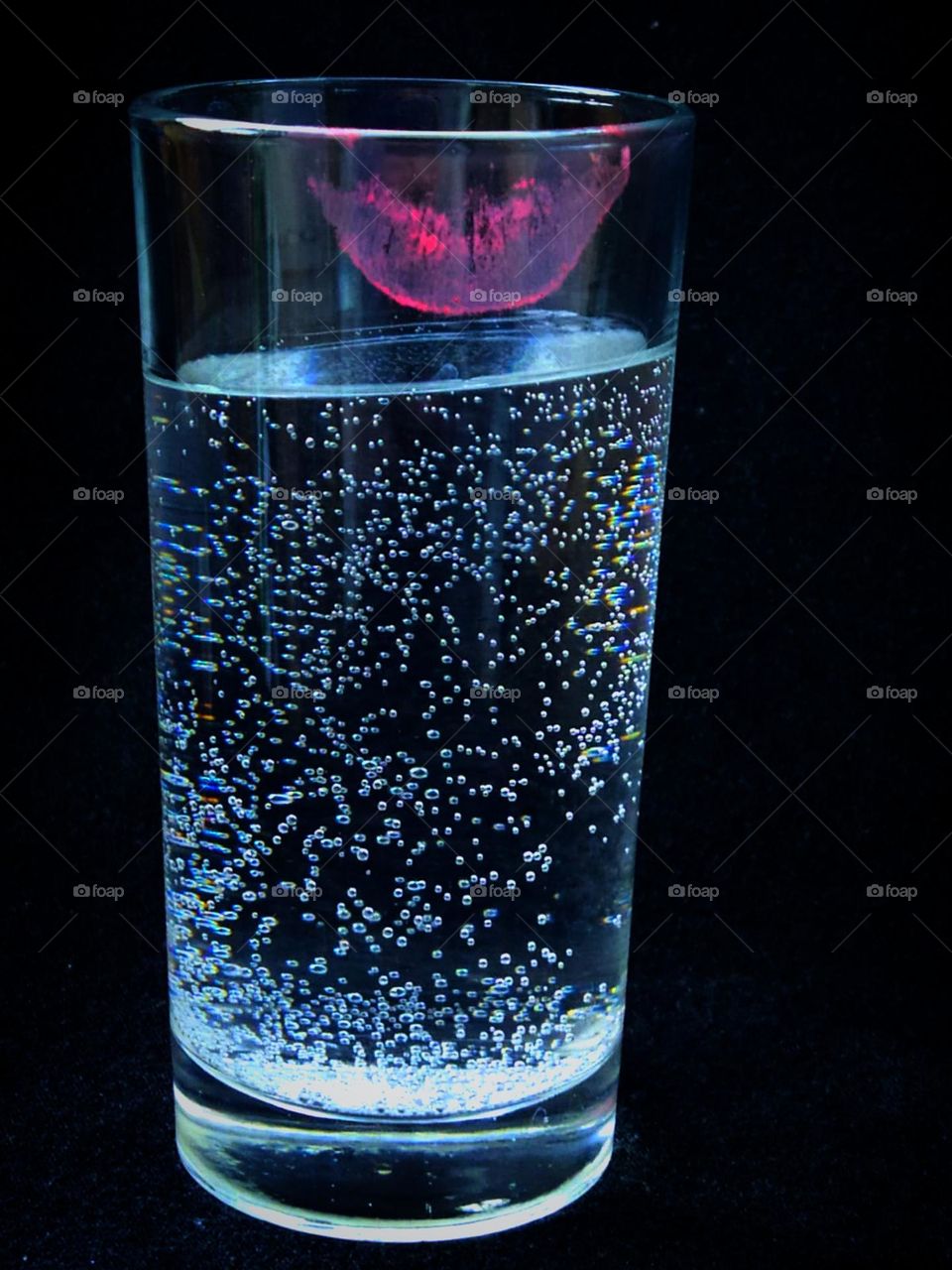 Transparent glass with sparkling water.  There is a trace of pink lipstick on the top of the glass.  Black background.