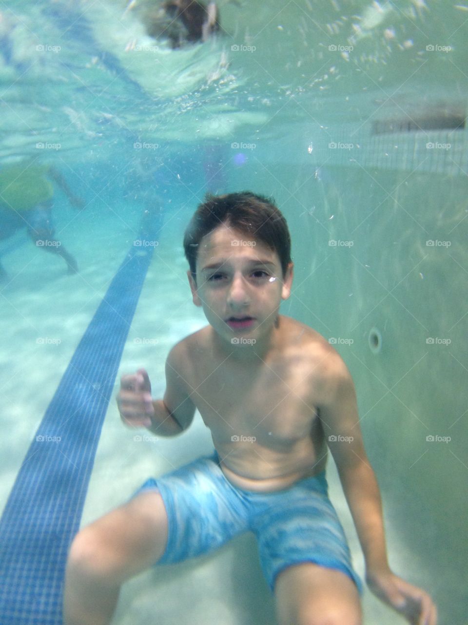 Come up for air. Underwater view of a boy sitting on the bottom of the pool