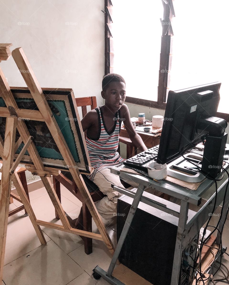 A child infront of a computer and a drawing easel by his side about to learn how to paint.