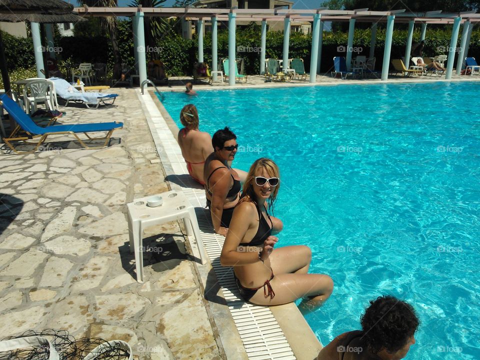 Smiling woman in bikini sitting near swimming pool in resort