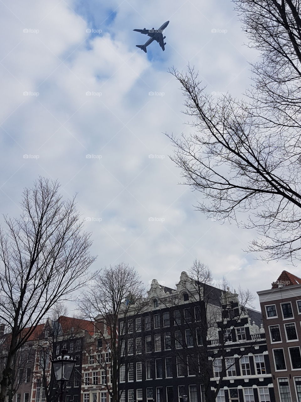 Vintage architecture roofs on buildings on an old alley street in Amsterdam, Holland, Europe. Airplane jet in clouds sky flying above