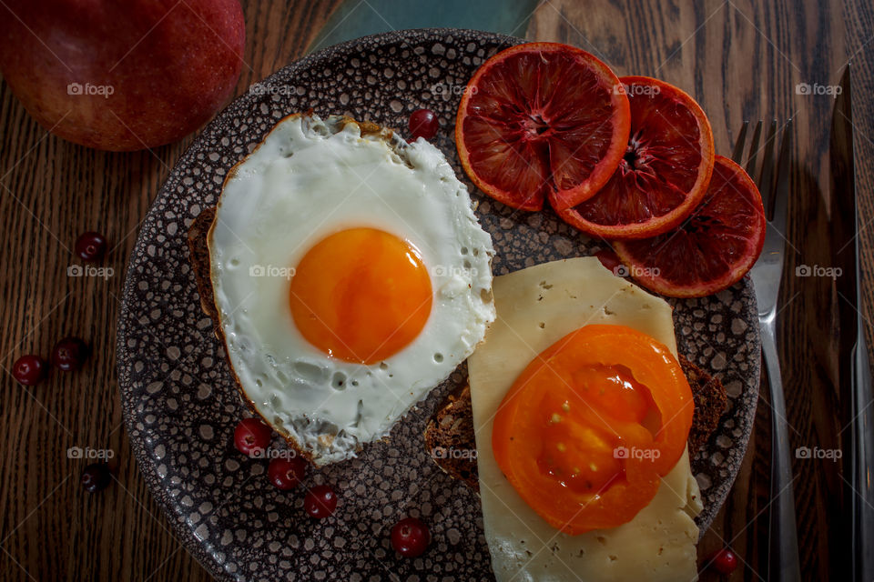 Grain bread with egg, tomato, cheese and bacon on ceramic plate with red orange to desert