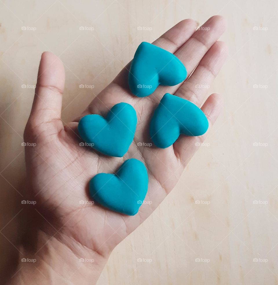 Blue heart shape of plasticine on hand against wooden background