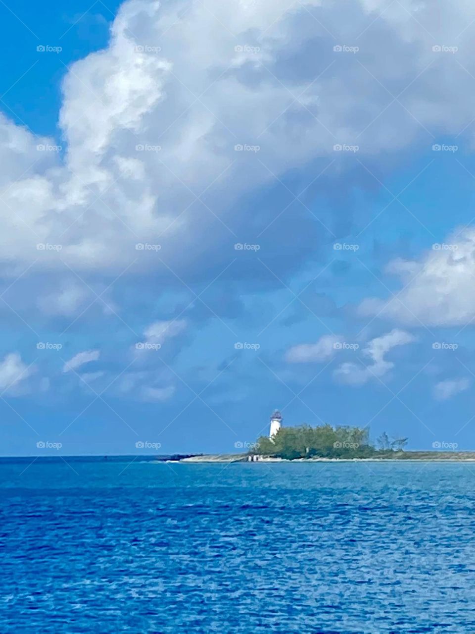 Pristine blue ocean water with island and lighthouse under a breathtakingly blue and white cloud-filled sky. 