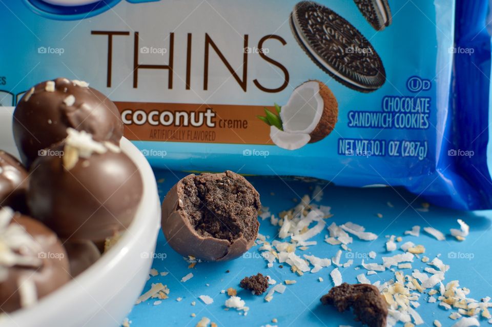 coconut Oreo thin cookies on a blue background with coconut shreds with truffles in a white bowl 