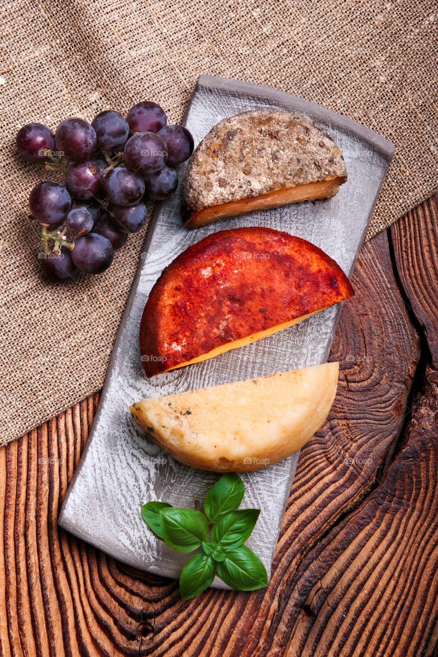 Cheese black grapes and olives decorated with mint on handmade pottery plates on old wooden table from above