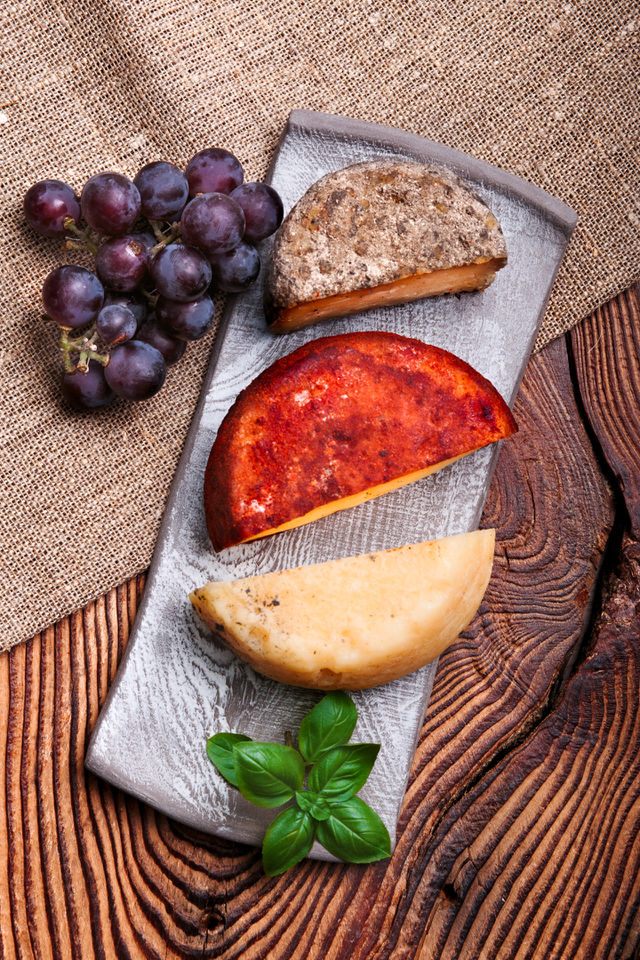 Cheese black grapes and olives decorated with mint on handmade pottery plates on old wooden table from above