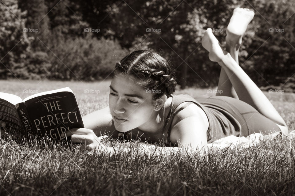 Girl is laying on the lawn reading a book