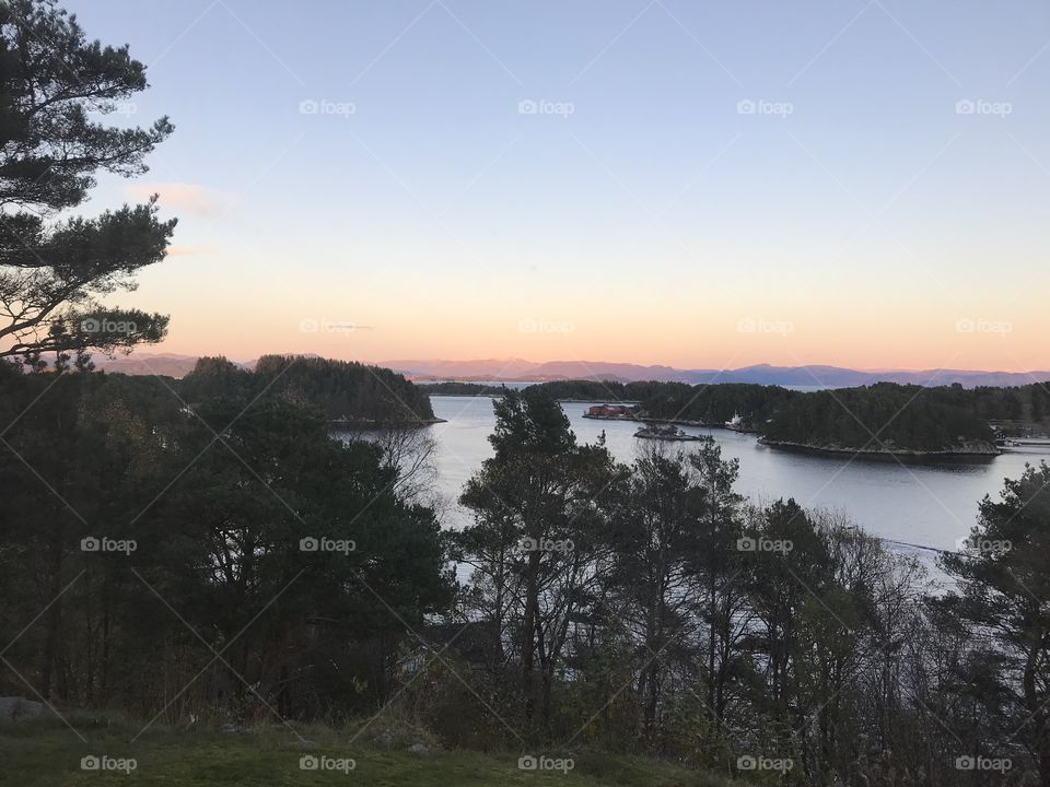 Landscape in Norway. The skies going from orange to blue with nice trees around and a ocean.