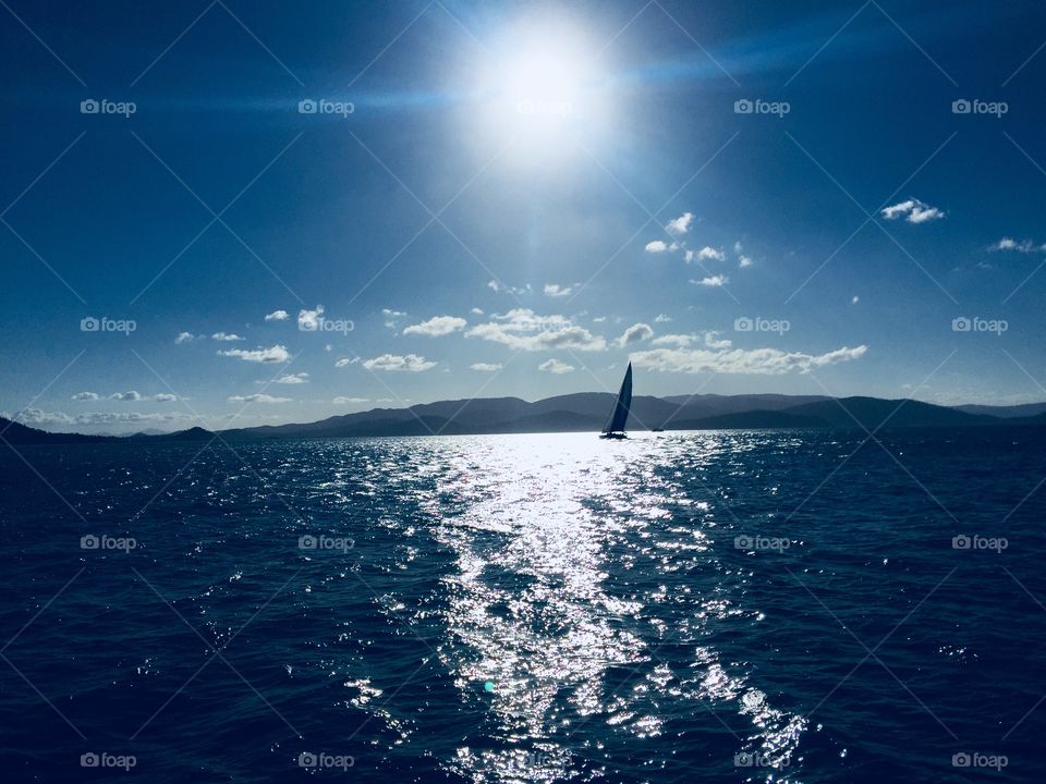 A lonely boat sails off into the sunshine in the Whitsundays of Australia