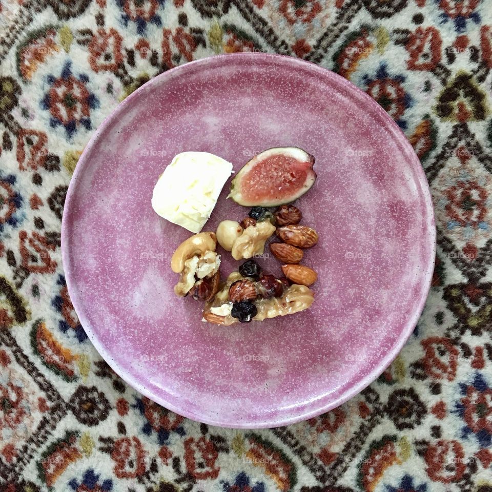 Fig, cheese and all kinds of nuts on a light purple plate sitting o a decorated carpet