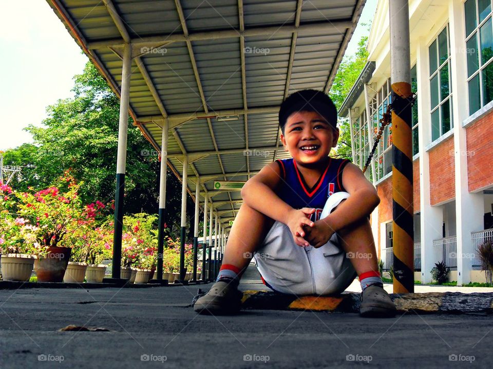 little asian boy resting under the shade of a covered hallway