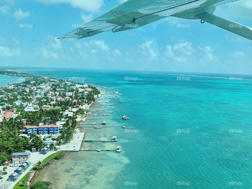 The view out of an airplane window showing the island and beautiful, blue ocean below the wing 