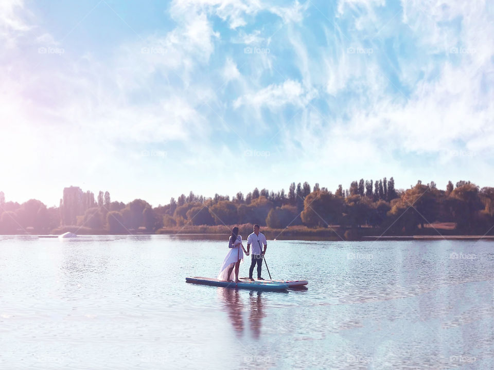 Couple in love holding hands and standing on the paddle boards in the middle of the lake 