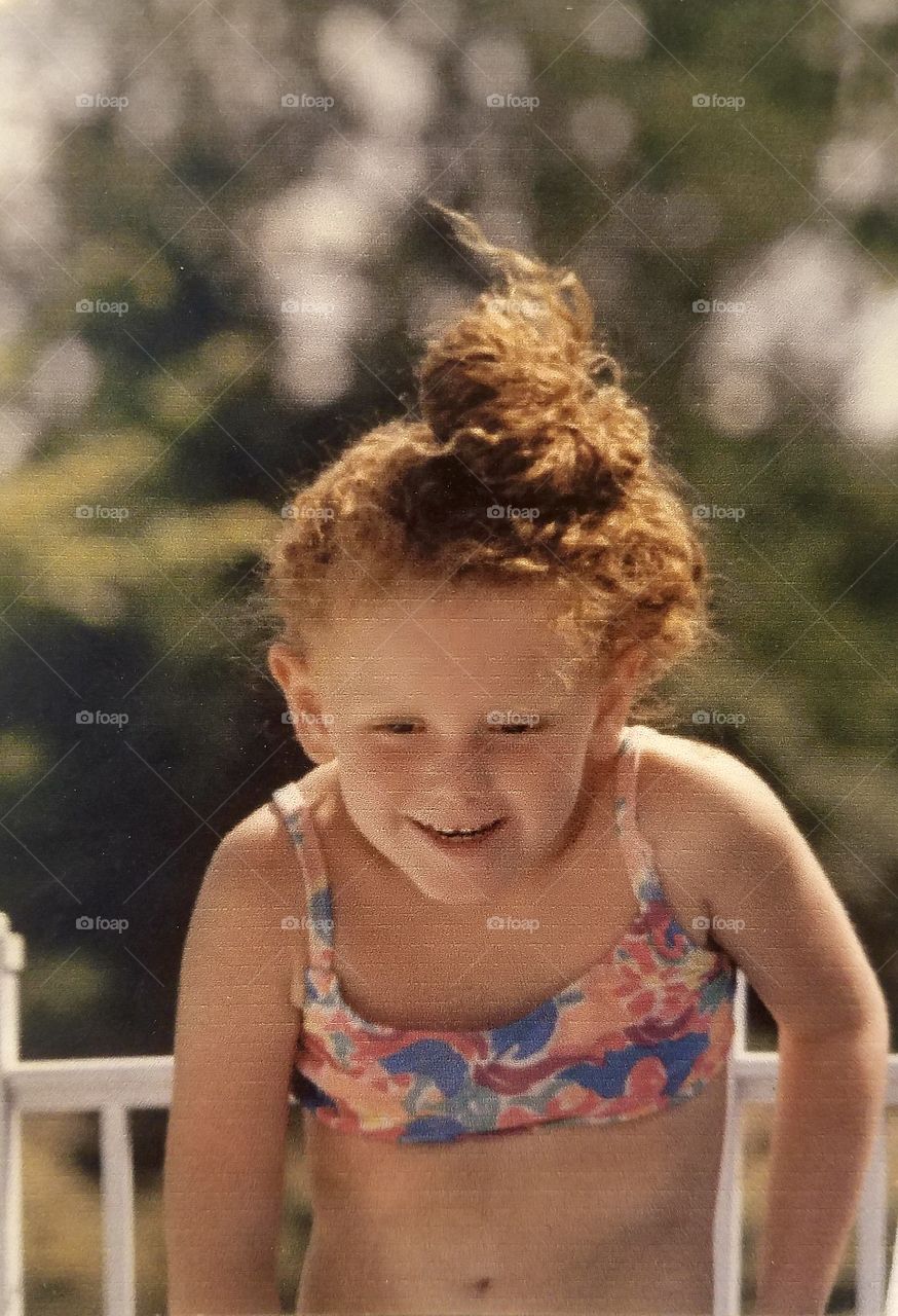Little redheaded girl with curly messy bun in swimsuit is about to jump into the pool.