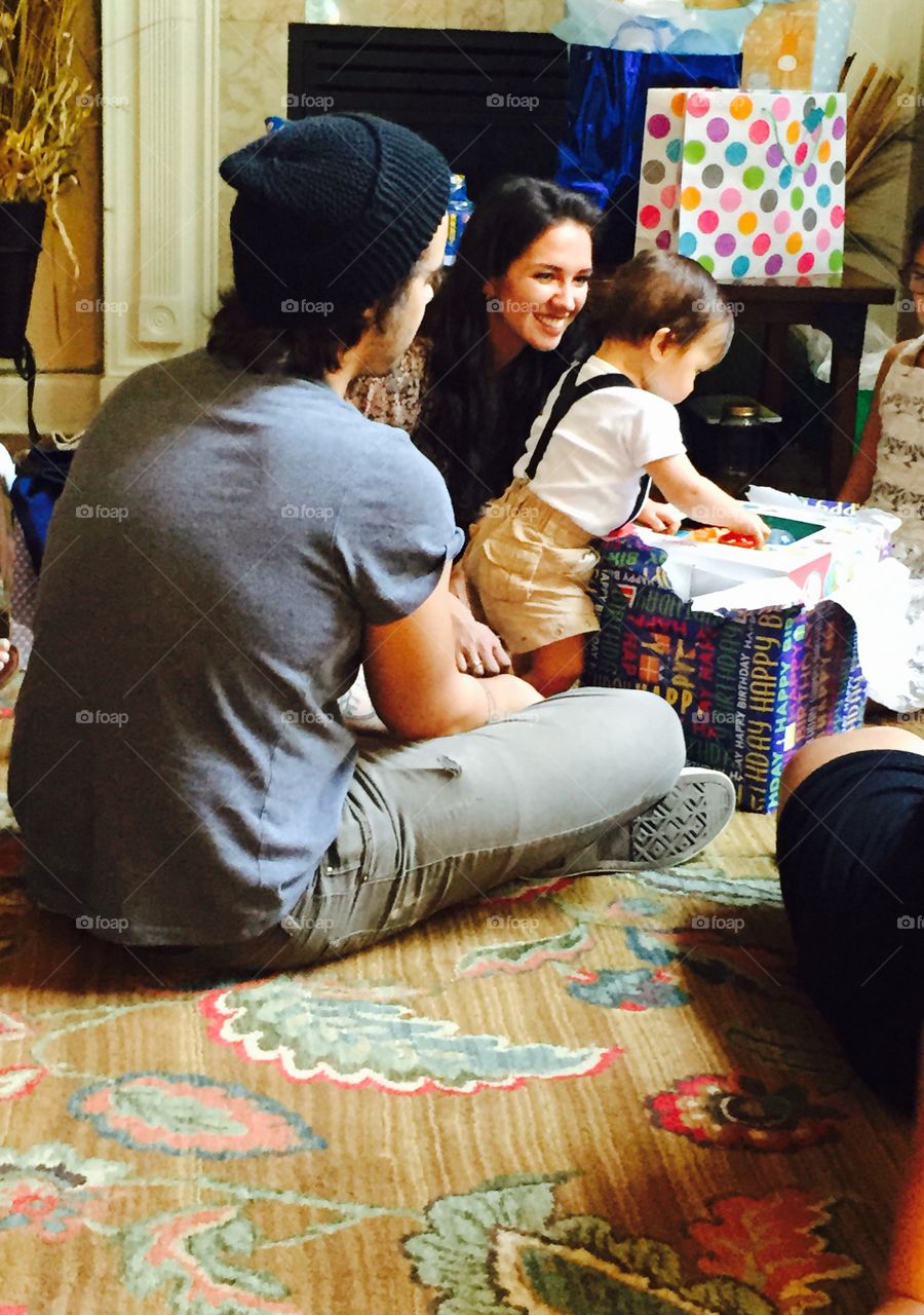 One year old boys first birthday party with his momma and daddy and about to open gifts from family. 
