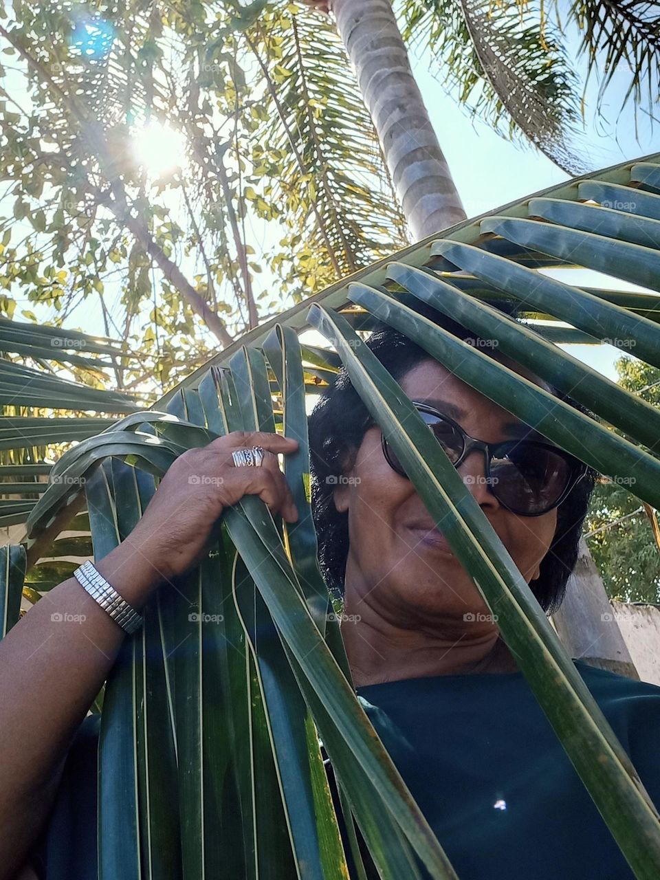 Senhora de pele negra, usando vestidos verde, numa tarde do Sol tímido;  brincando com as folhas da Palmeira