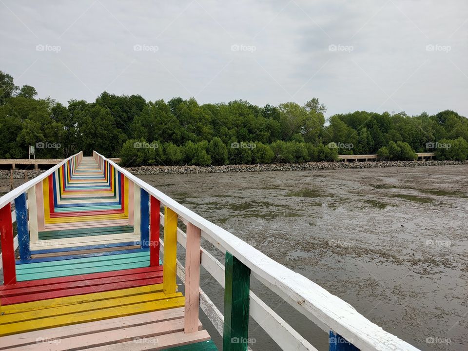 A wooden bridge painted like a rainbow making a path to the sea.