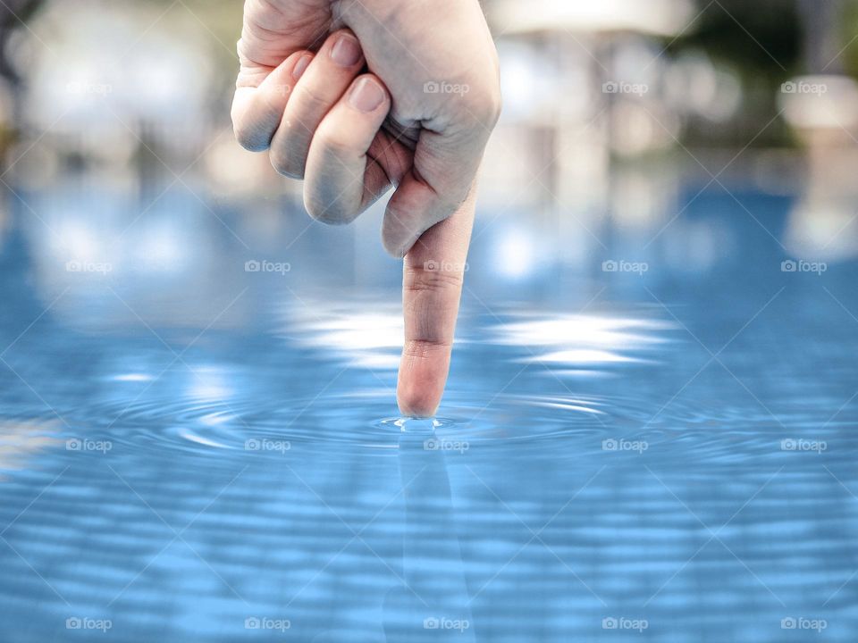 A finger testing the water temperature before entering the swimming pool