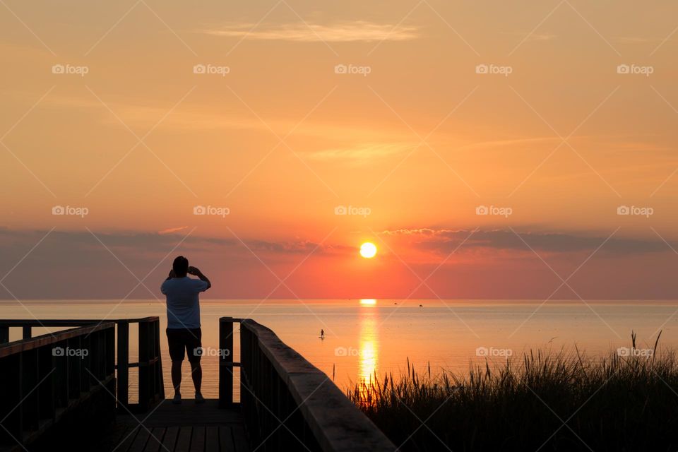 Man taking pictures of a colorful sunset by the ocean 