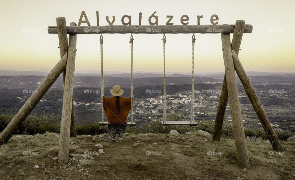 A woman sits on the swings overlooking the Portuguese town of Alvaiazere around sunset