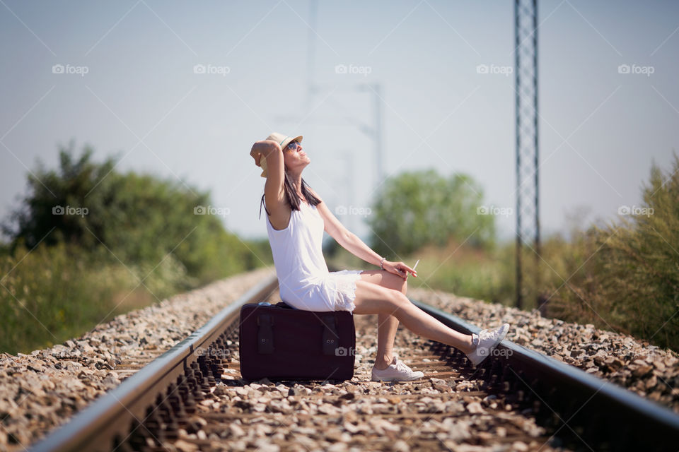 Woman sitting on empty rail track with bag smoking cigarette