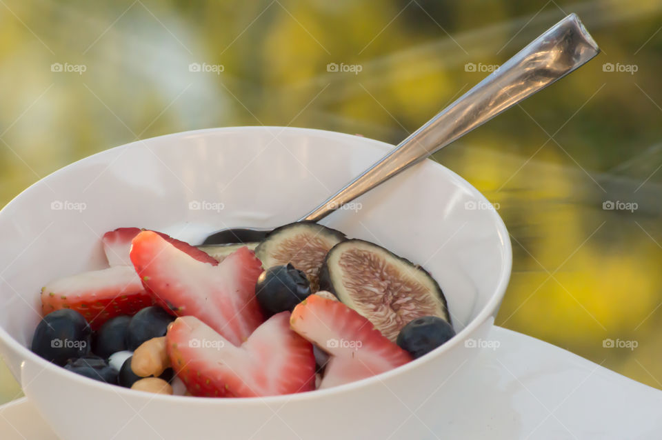 Fresh fruit and yogurt smoothie bowl outdoors with heart shaped strawberry, blueberry, fig and cashews and almond with honey on top closeup healthy lifestyle antioxidant background 