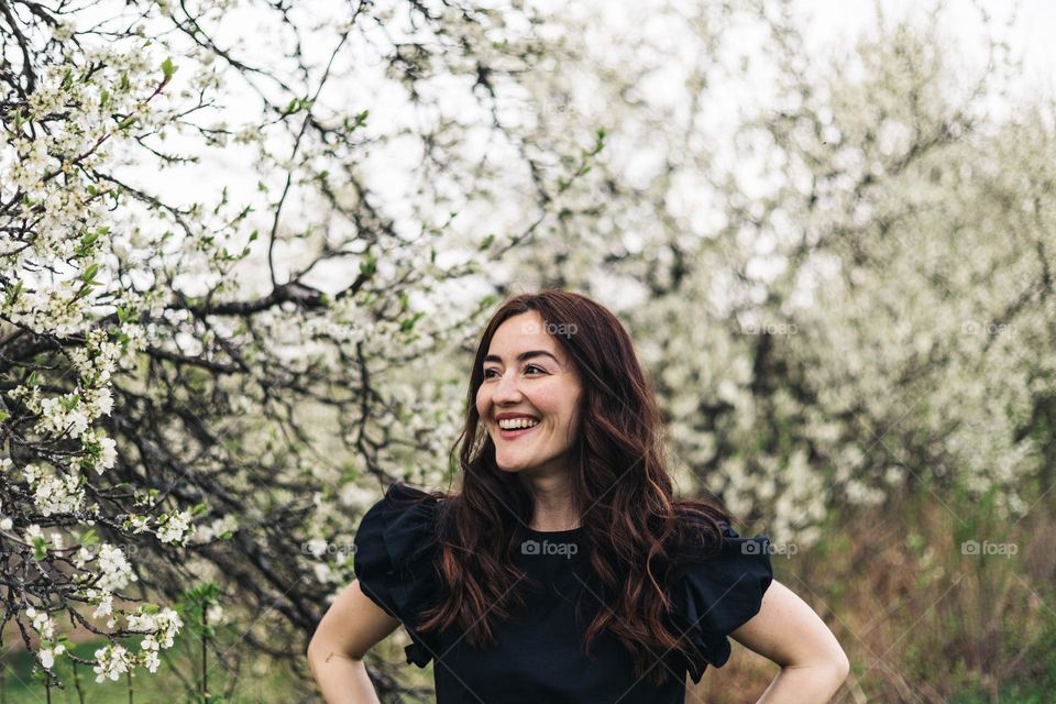 Happy smiling woman surrounded by blossoming trees in spring time.
