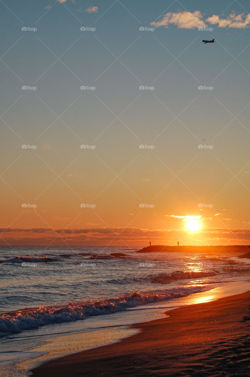 Landscape of a beach during sunset with fishermen and plane on the background 