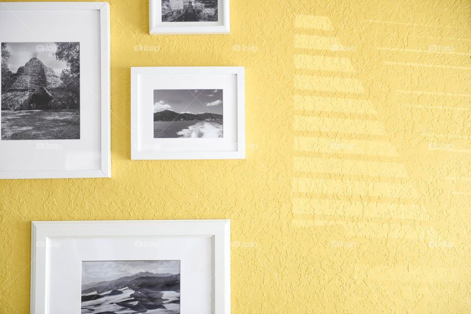 Rectangular picture frames hanging on a yellow wall with the shadow of window blinds