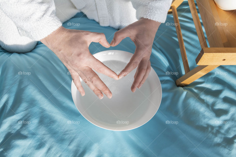 A man at home takes care of himself and does a manicure at home on a blue background and with orange.