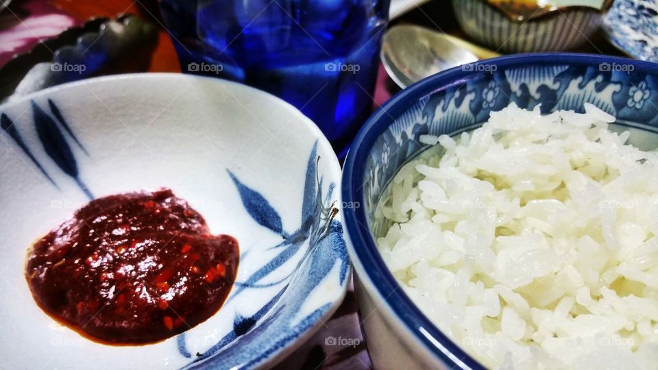 A bowl of freshly cooked white boiled rice next to a dish containing some chilli paste, or Gochujang in Korean.