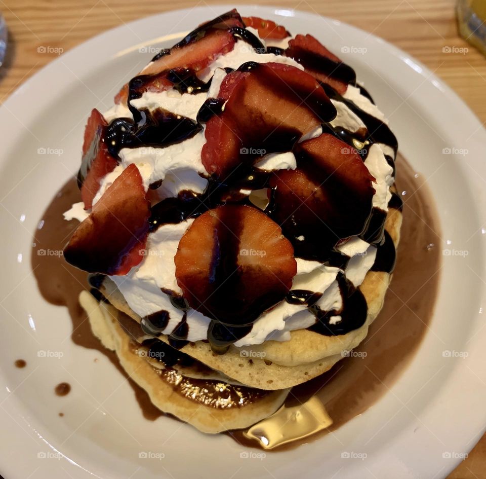Pile of pancakes decorated with strawberries, chocolate and whipped cream seen from above, yummy and delicious breakfast, American food, American breakfast