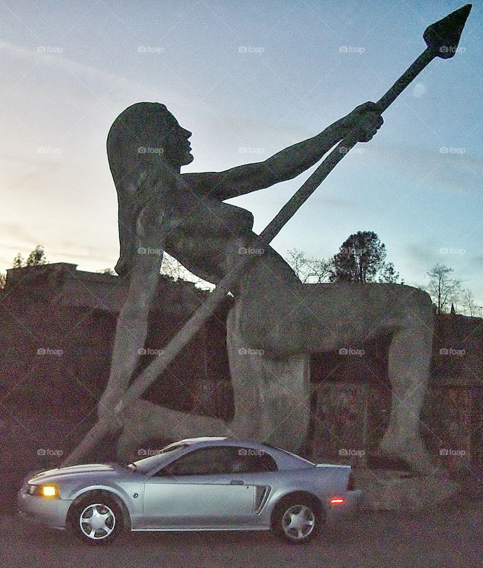 Ford mustang by a huge statue of a female warrior