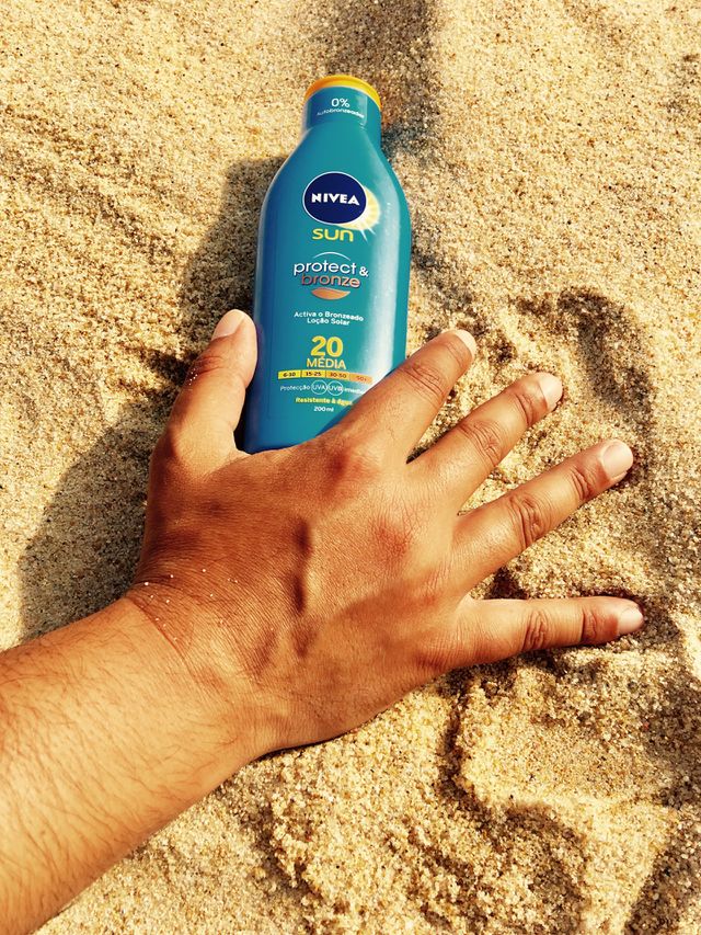 Hand holding bottle of Nivea Sunscreen Protector in the beach’s sand 