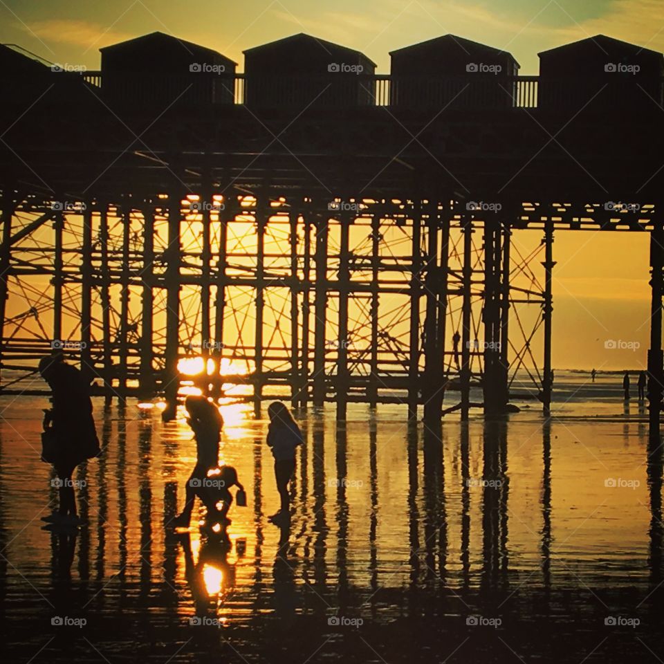 A family paddles under Hastings pier at sunset