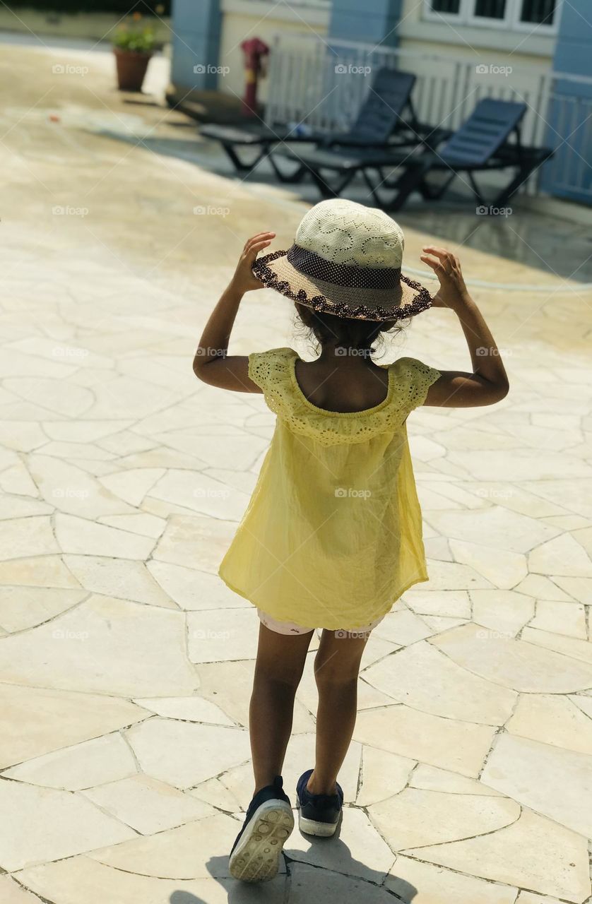 A little girl in a yellow summer outfits and hat on her head .
