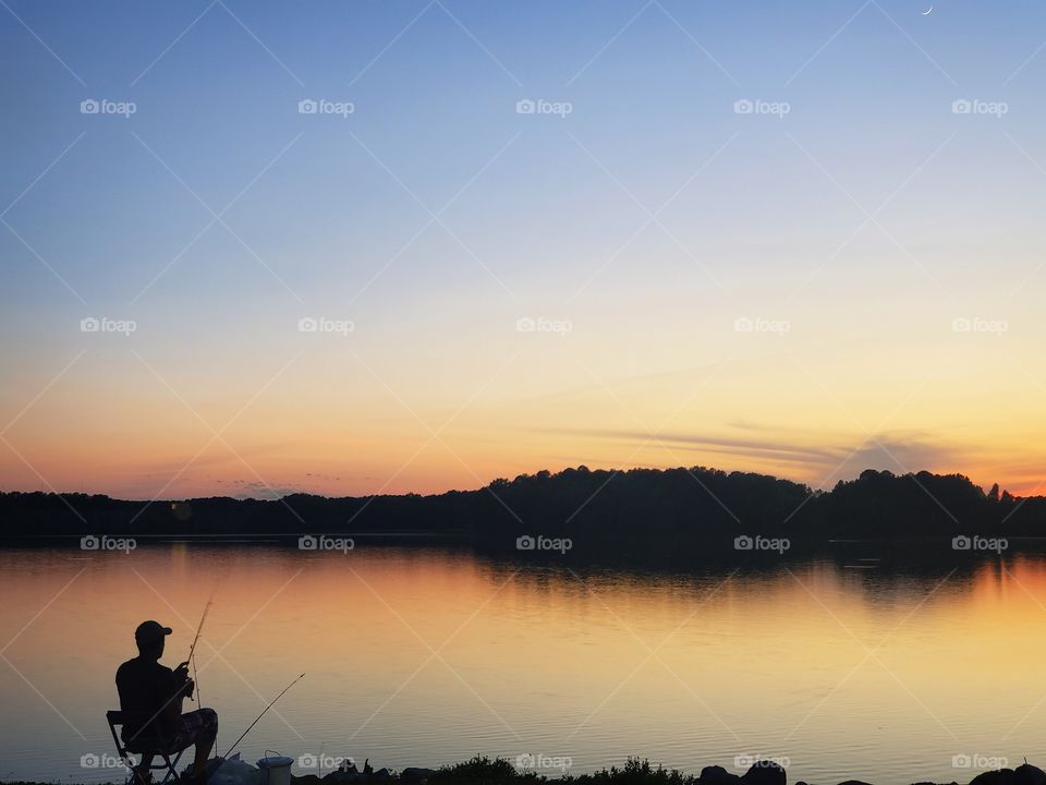 man fishing on river bank at sunset