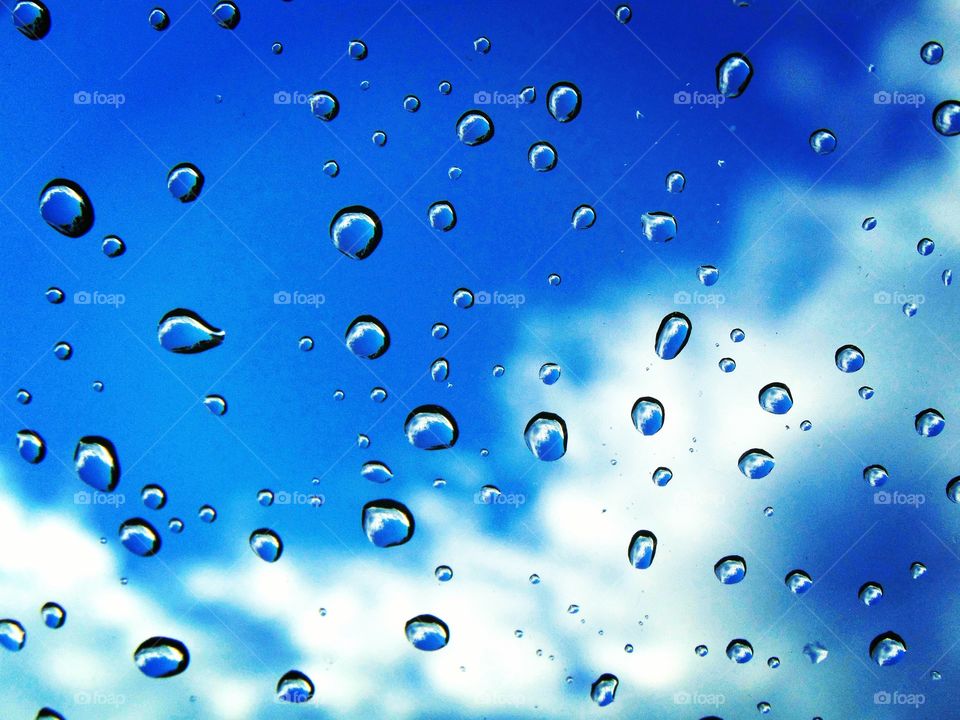 Random photo of raindrops on a windshield with cloudy sky in background.