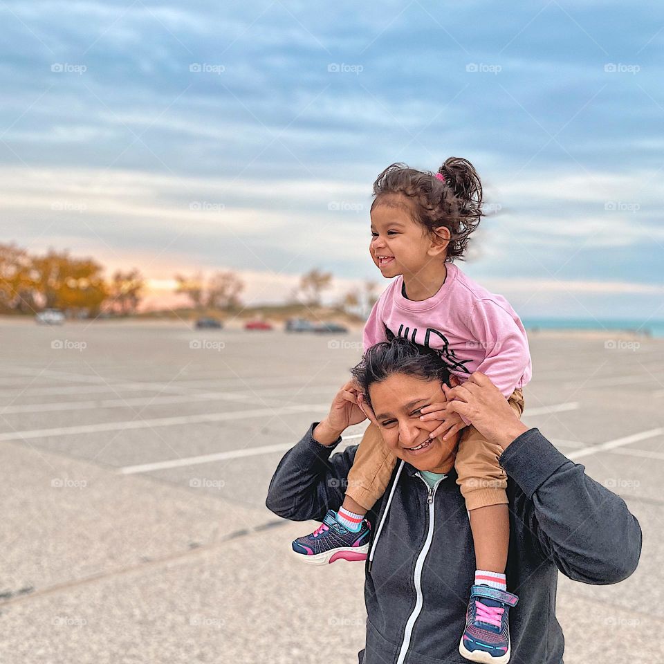 Toddler and mother at the beach, pure joy on the faces of mother and child, loving the beach, happiness on vacation, mother gives toddler a ride on her shoulders, smiling like crazy, smiling with happiness, family time fun at the beach 