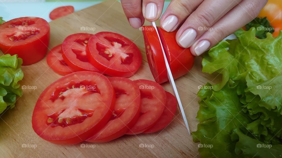 Cutting red tomatoes into slices for salad. Lunch time.