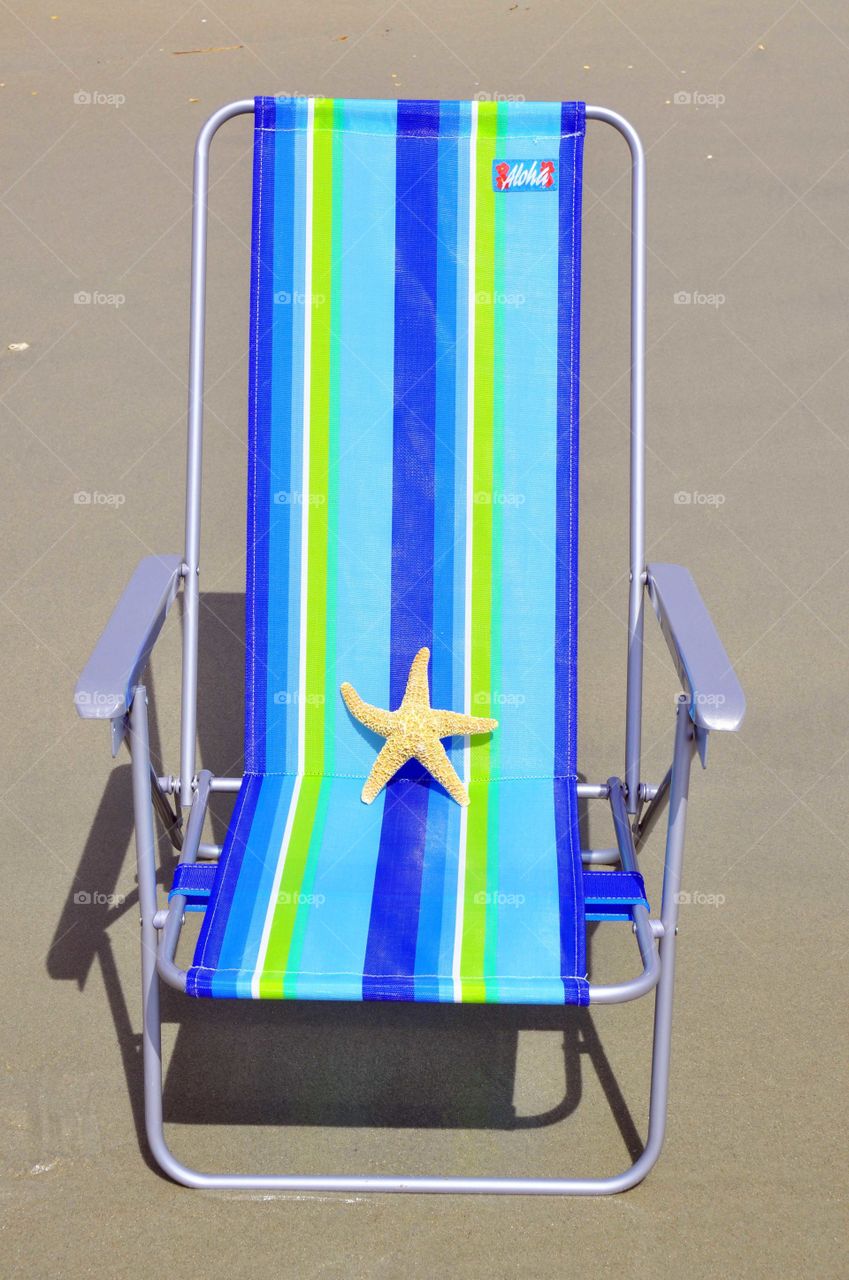 Beach chair. A pretty  striped beach chair sits with a starfish on it at the beach