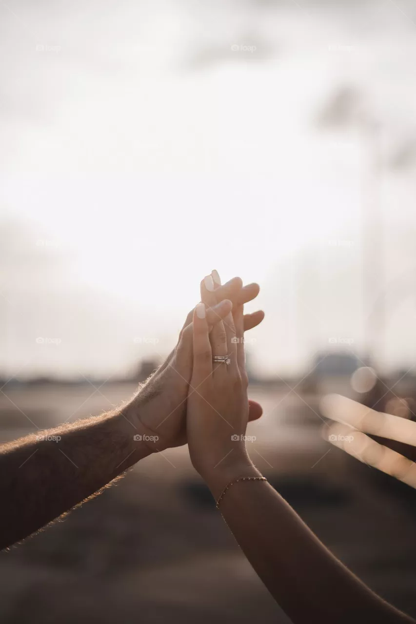 Two hands of an edgy married couple on the rooftop of a garage during sunset hour. Beautiful backlit.