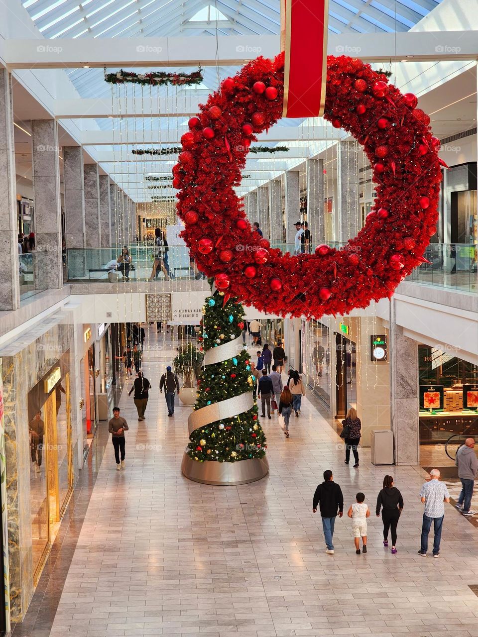 A shopping mall is prepared for the Christmas holiday season with brightly colored wreaths and Christmas trees