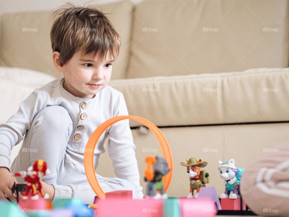 Cute toddler boy in grey pajamas playing with toys