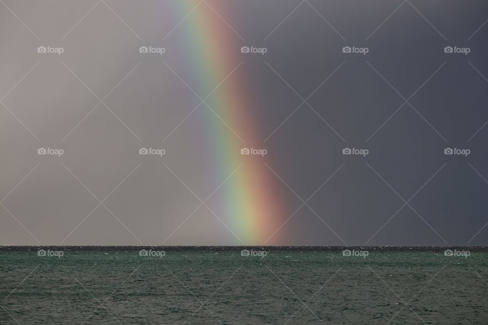 Brilliant rainbow arching into a dark choppy ocean during storm