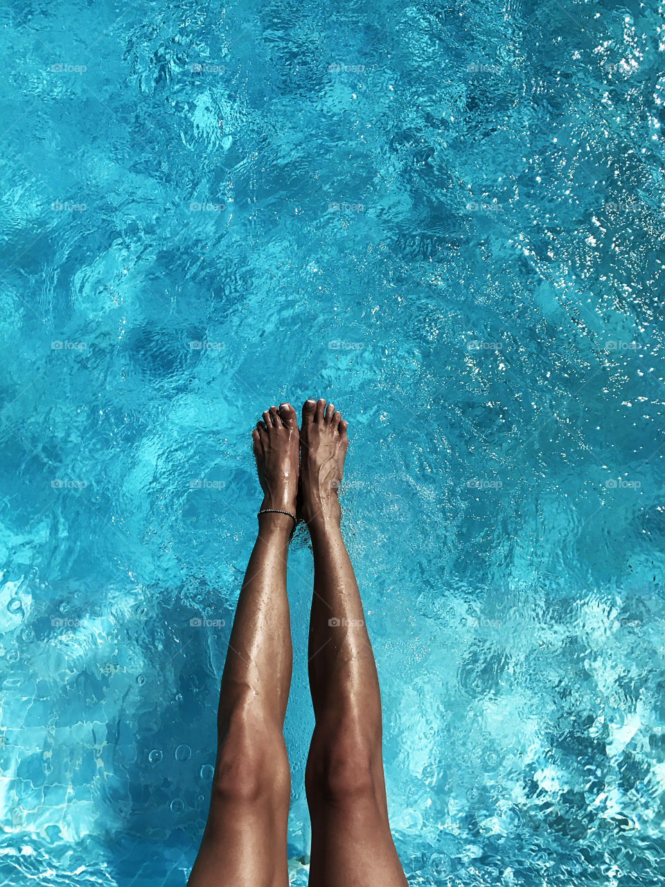 Female feet under the blue water of swimming pool 
