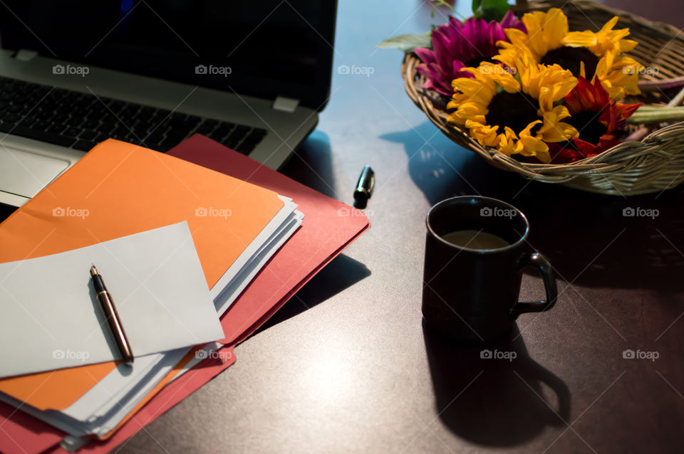 Sunflower floral centerpiece on desk with laptop, files with paper, fountain pen and cup of coffee elevated view conceptual work life balance tranquil business scene