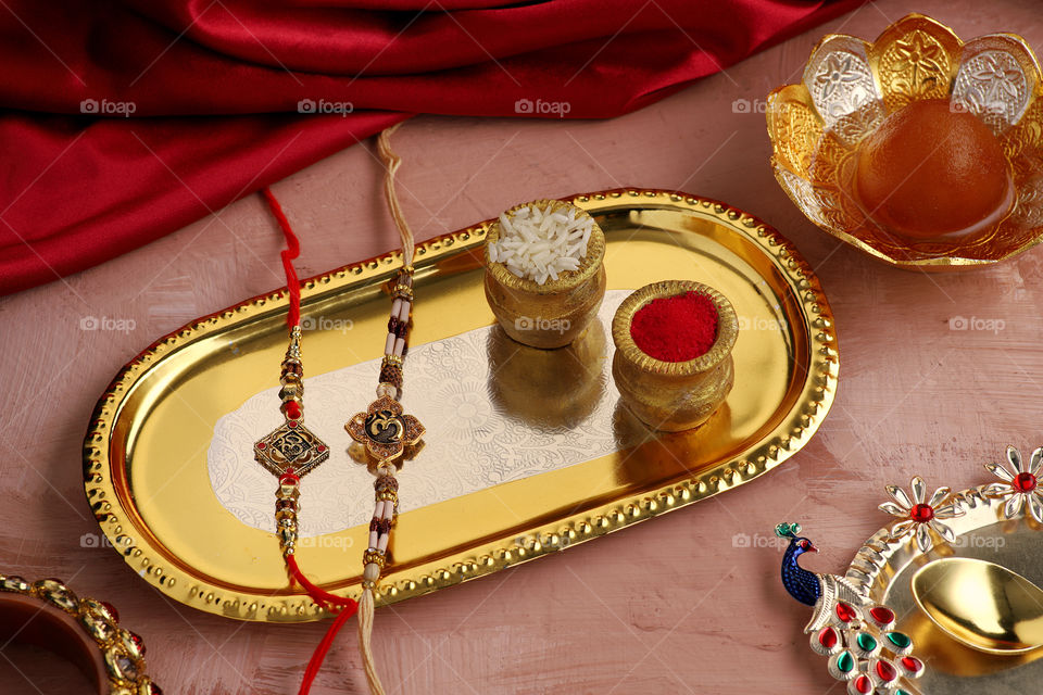 Indian traditional rakhi on a gold silver tray with rice, kumkum and sweets